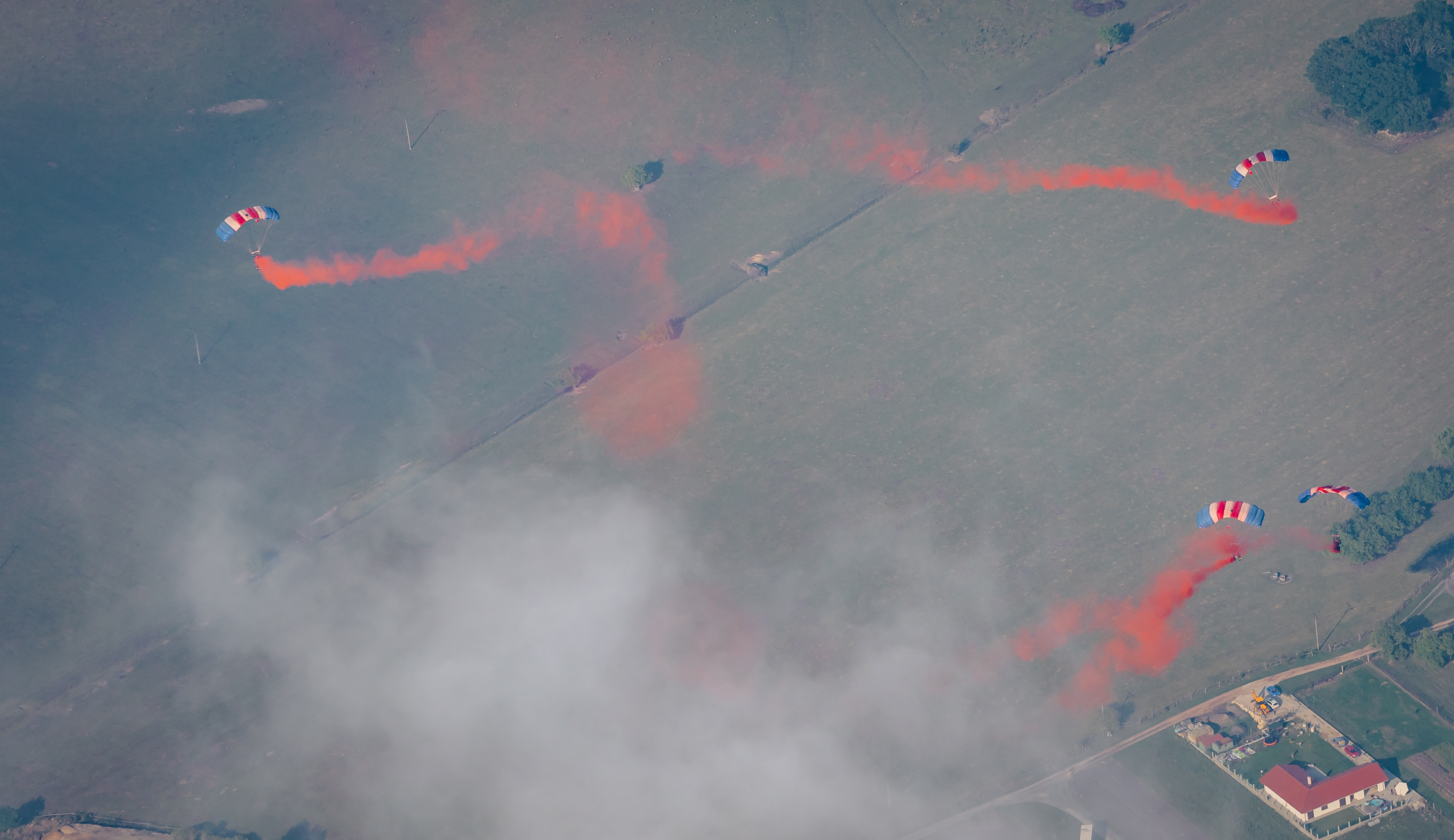 Image shows RAF Falcons team falling with parachutes deployed and red smoke trails.